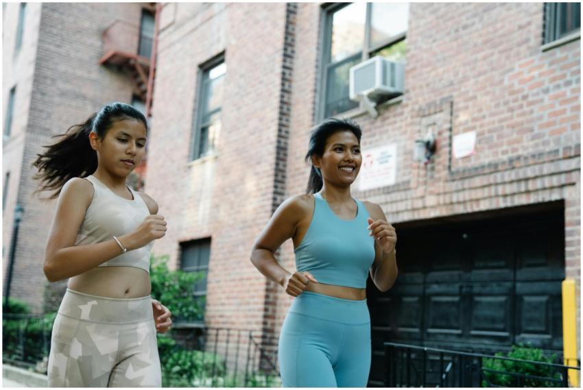 Two women jogging outdoors in sportswear through a