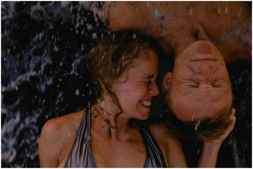 Joyful couple embracing beach waves, eyes closed,