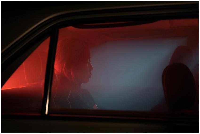A woman sitting in a car, silhouetted against atmo