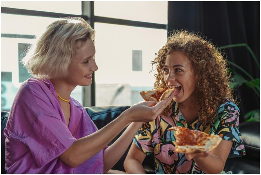 Happy couple sharing pizza slices indoors, showing
