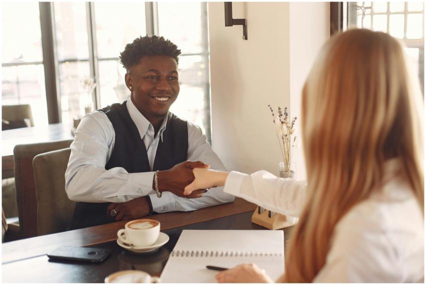 Two adults shaking hands across a table in a coffe