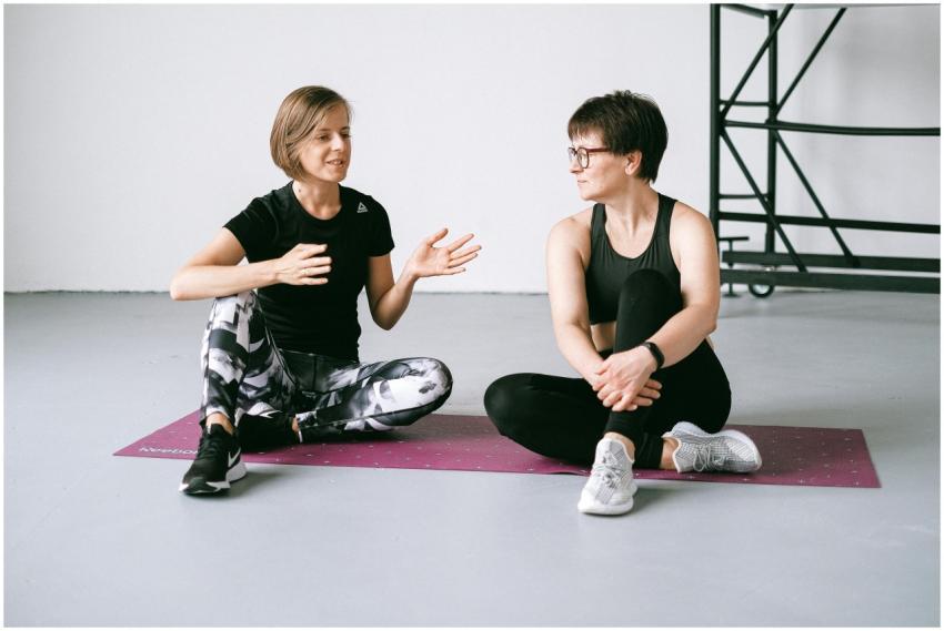 Two women talking while sitting on yoga mats, focu