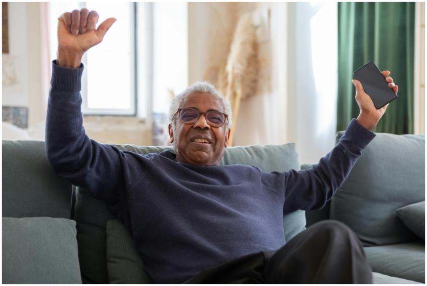 Senior man joyfully sitting on a couch holding a s