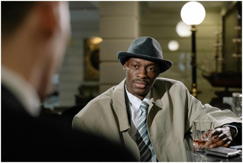 A detective in a trench coat and fedora at a bar,