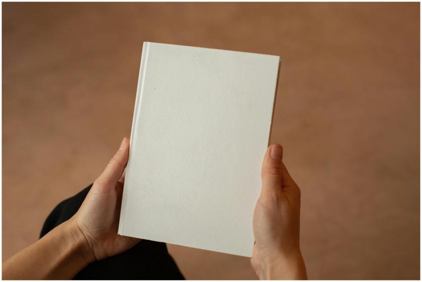 A person holding a blank hardcover book. Perfect f