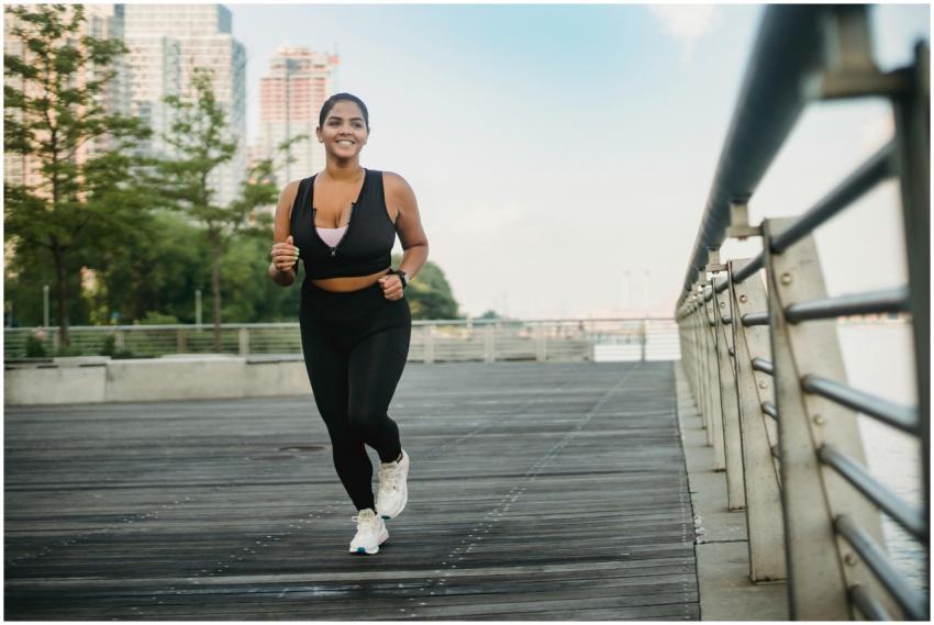 A woman in activewear jogging on a boardwalk by th