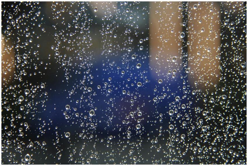 Macro shot capturing raindrops on glass with a blu