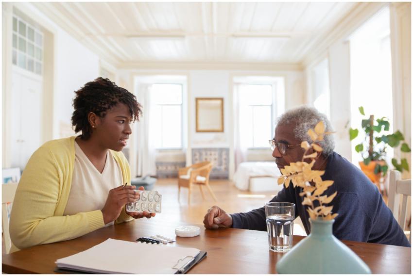 An elderly man sits with a caregiver discussing me