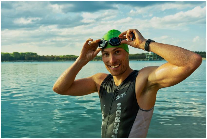 Confident male athlete adjusting goggles at a lake