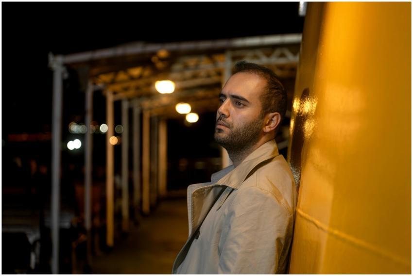A contemplative man in a trench coat leans against