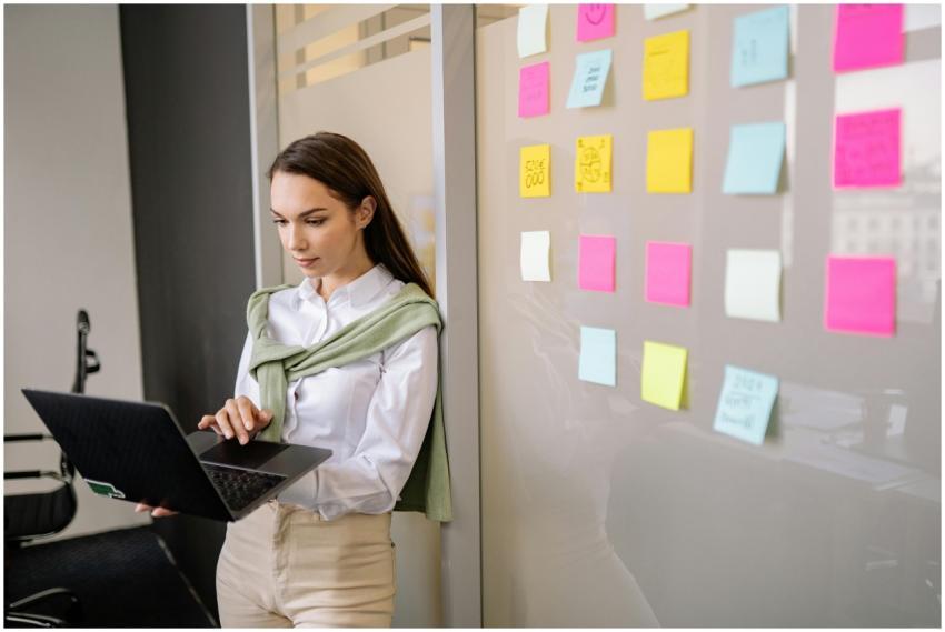 A young woman uses a laptop while standing by a wa