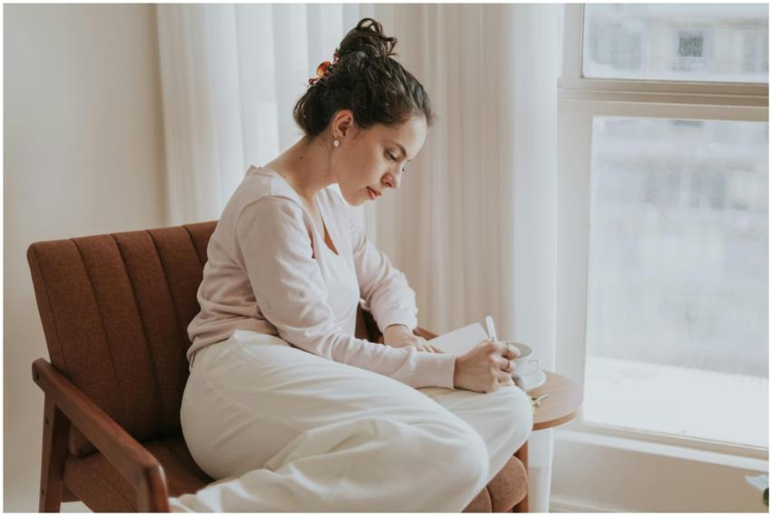 A woman comfortably journaling by a window, surrou