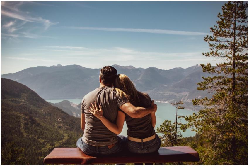 Couple sitting on bench embracing scenic mountain