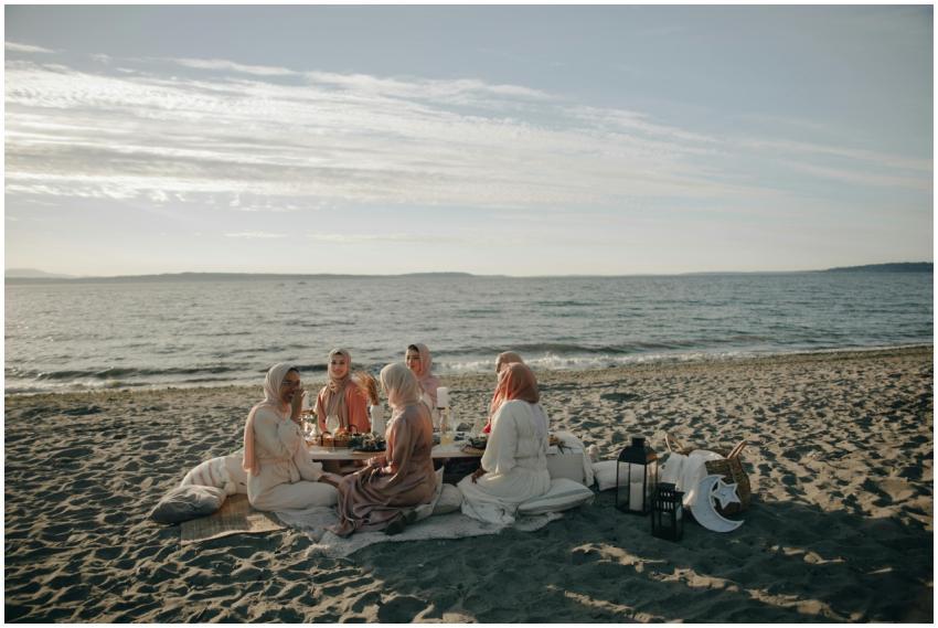 Five women in hijabs having a beach picnic with th