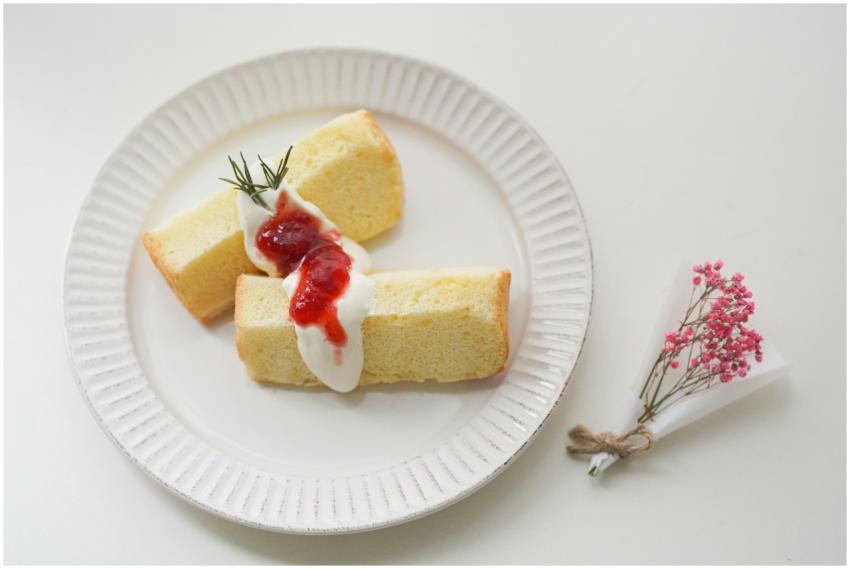 Two slices of sponge cake topped with cream and ja