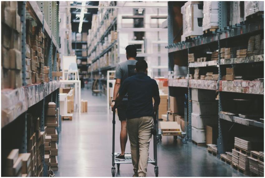 Two men maneuver a trolley in a large warehouse fi