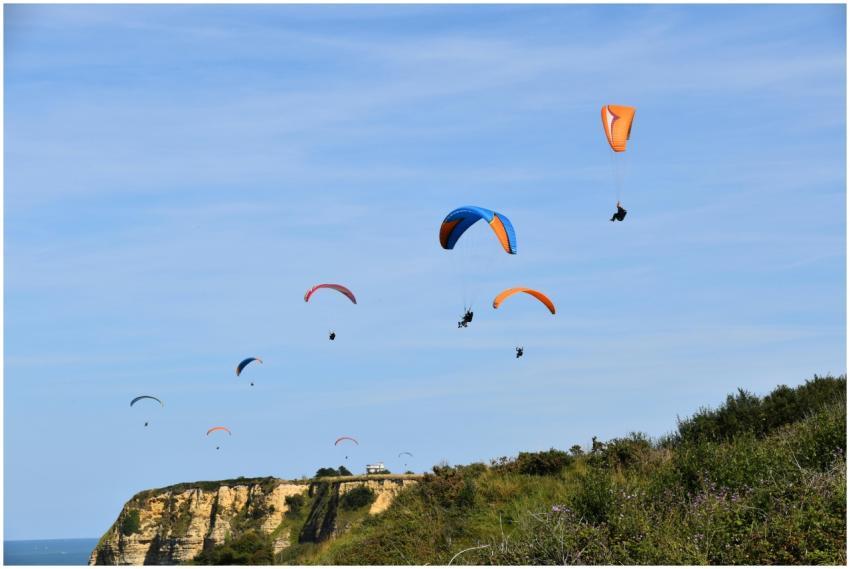 A group of paragliders soar over scenic cliffs on