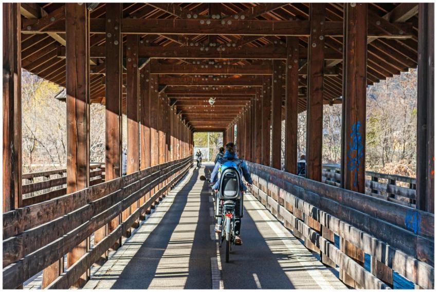 Cyclists ride through a scenic covered wooden brid