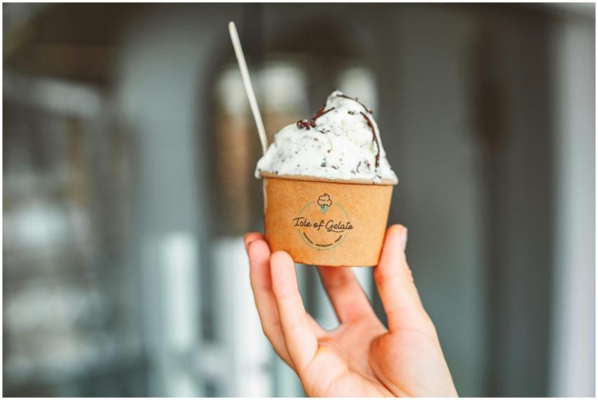 A hand holding a cup of creamy gelato with a spoon