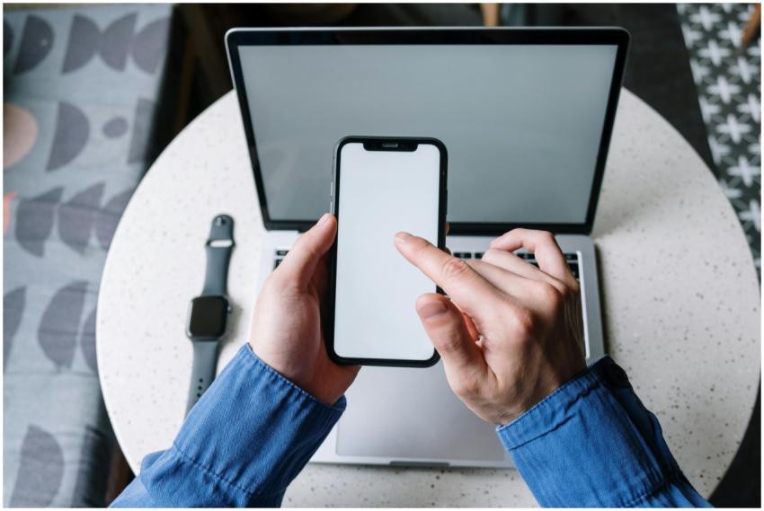 Hands operating a smartphone above a laptop with a