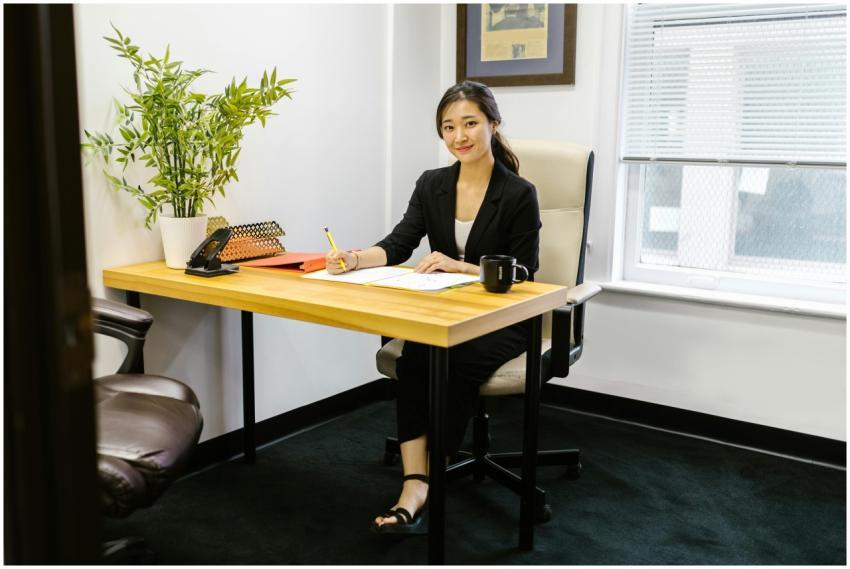 An Asian woman in business attire writing at a des
