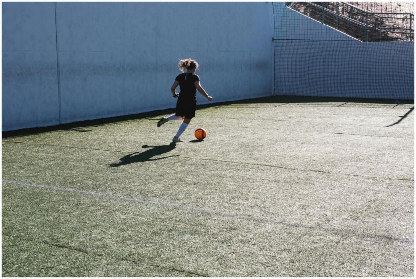 A young woman playing soccer, dribbling a ball on