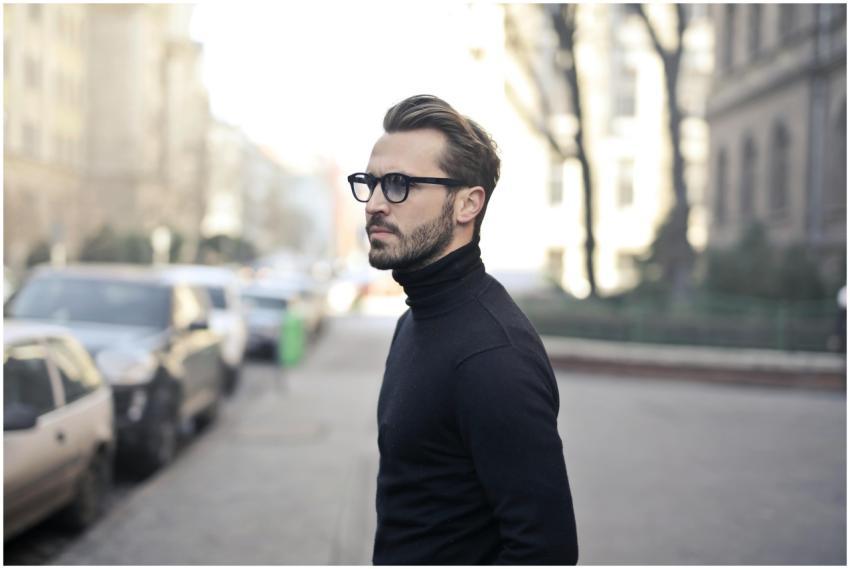 A fashionable man in a black top and glasses poses