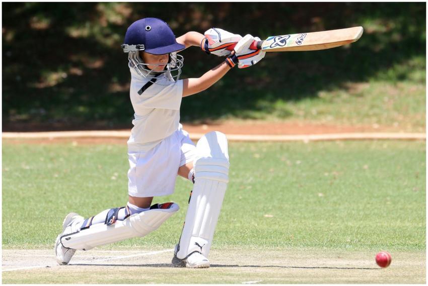 A young boy playing cricket, executing a classic s