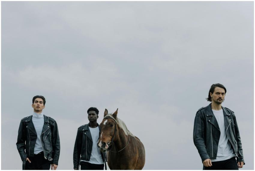 Three men wearing leather jackets stand with a hor