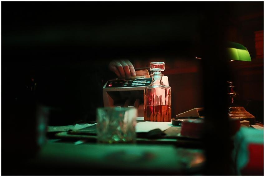 A dimly lit bar scene with whiskey, cash counting,