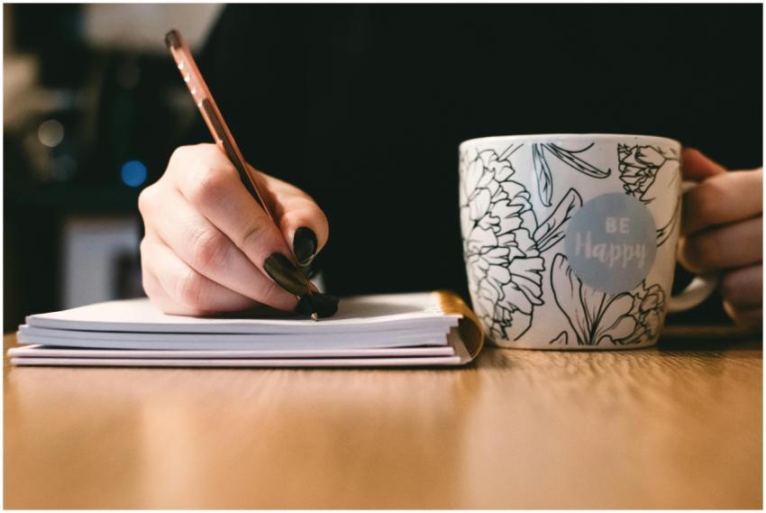 Person writing in a notebook with a floral ceramic