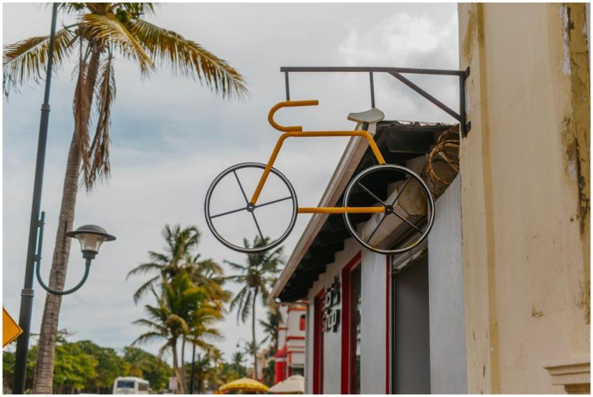 A vintage bicycle sign hangs on a building in a tr