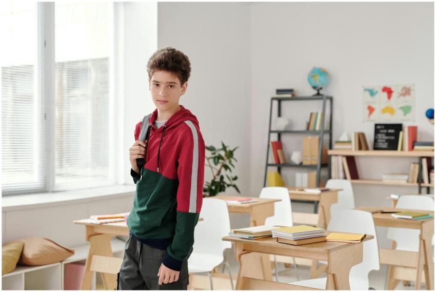 A teenage boy in a hoodie stands in a bright class