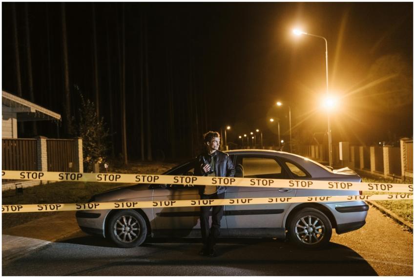 Man stands behind a car and stop tape at night, cr