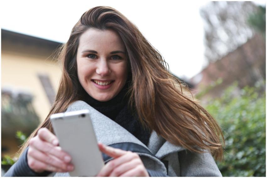 A young woman happily uses her smartphone outside,