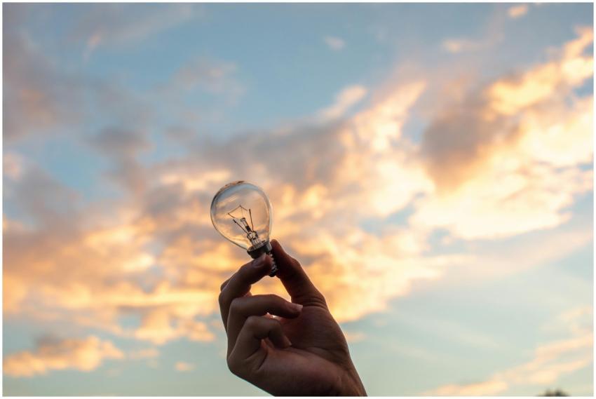 A hand holds a light bulb against a scenic sunset