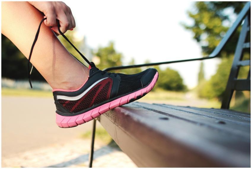 A woman laces her sneakers on a park bench, prepar