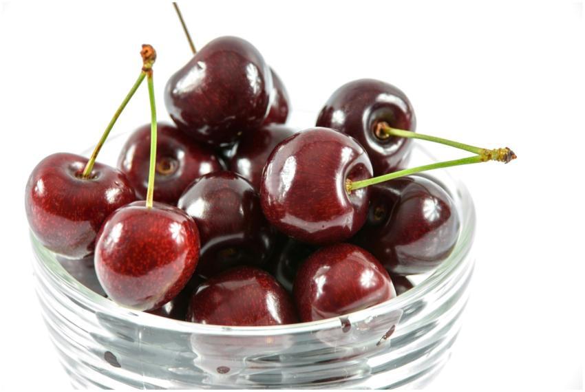 Glossy red cherries in a clear glass bowl on a whi
