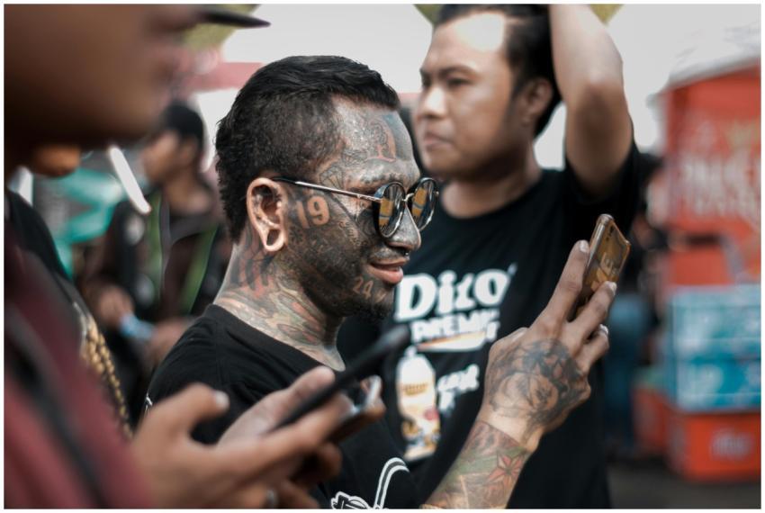 A tattooed man uses a smartphone while standing in