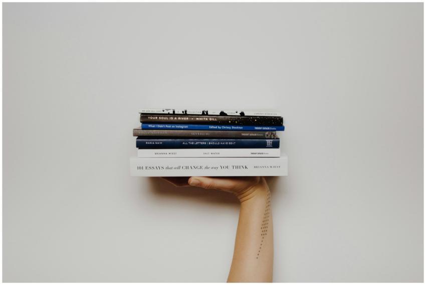 Hand holding a stack of books against a minimal wh