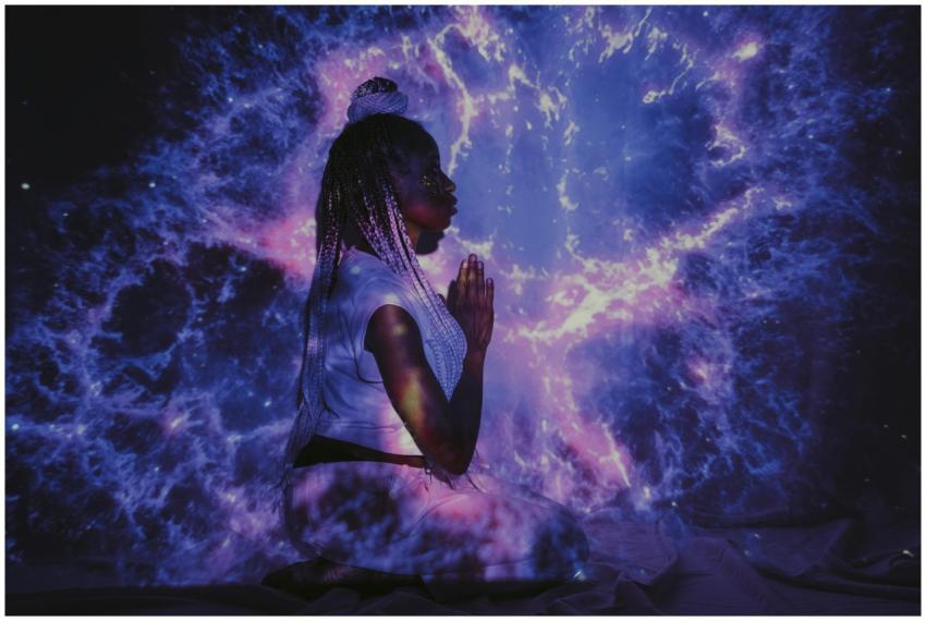 A woman kneels in a galaxy projection, creating a