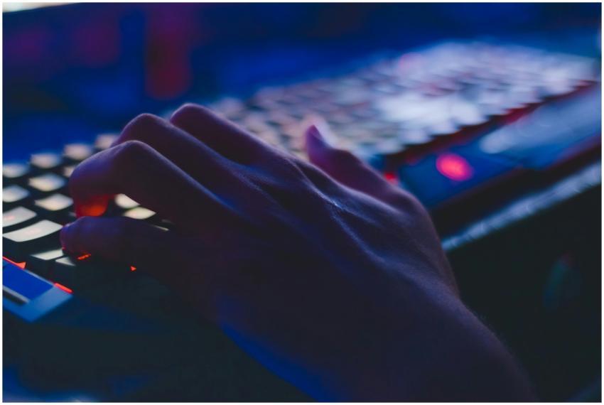 A hand typing on a glowing keyboard in dim lightin