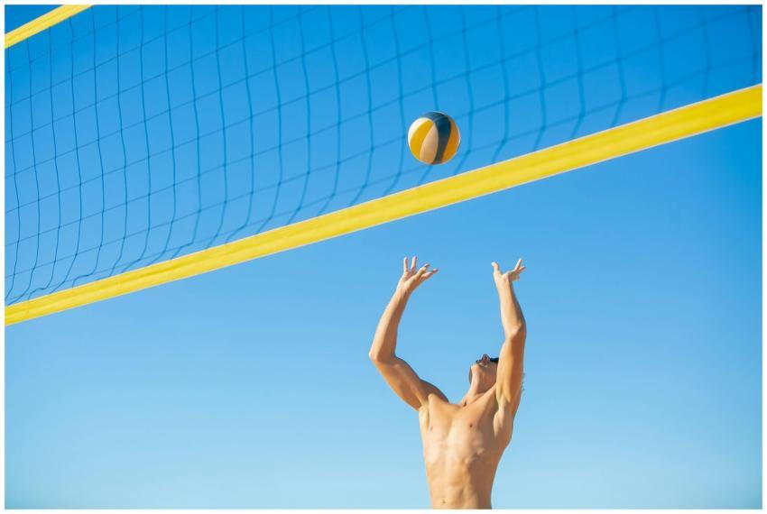 A shirtless man playing beach volleyball under cle