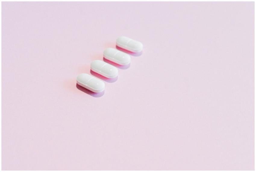 Four white pills arranged on a soft pink surface,
