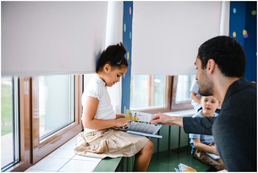 A teacher helps a young girl read a book with fell