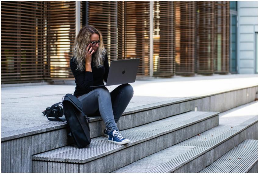 A woman working remotely on laptop outdoors, weari