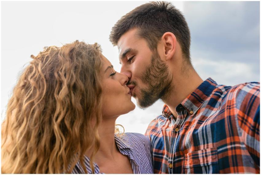 A young couple kisses passionately against an outd