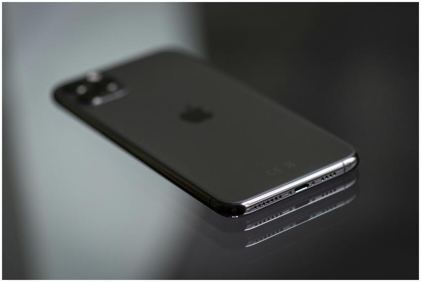 Close-up of a black smartphone on a shiny reflecti