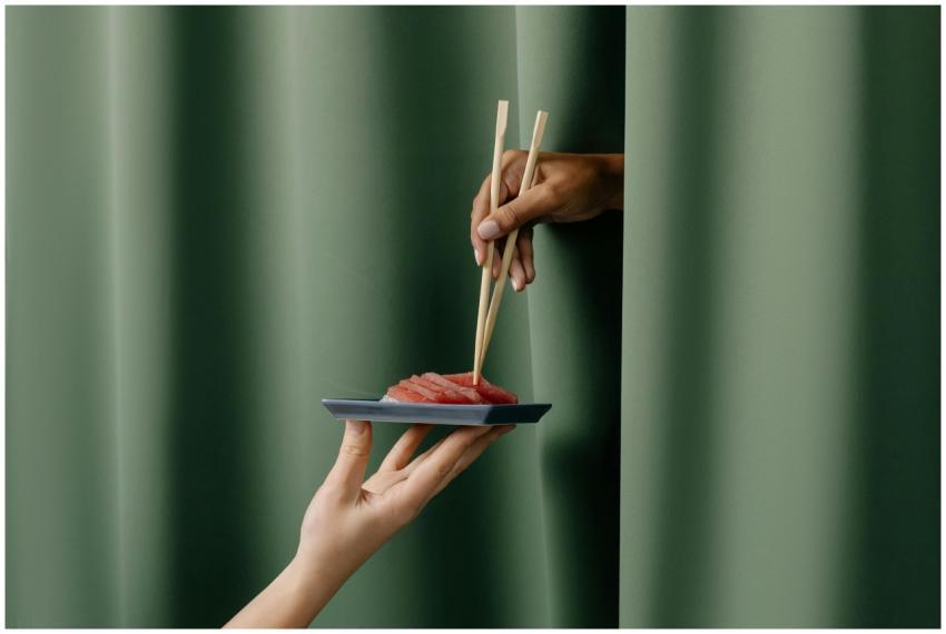 Two hands with chopsticks and sashimi on a plate i