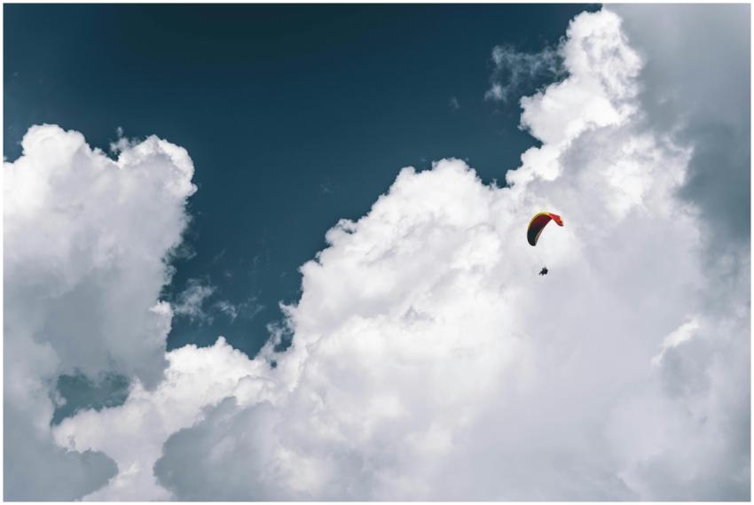 A paraglider flying high in the expansive sky surr